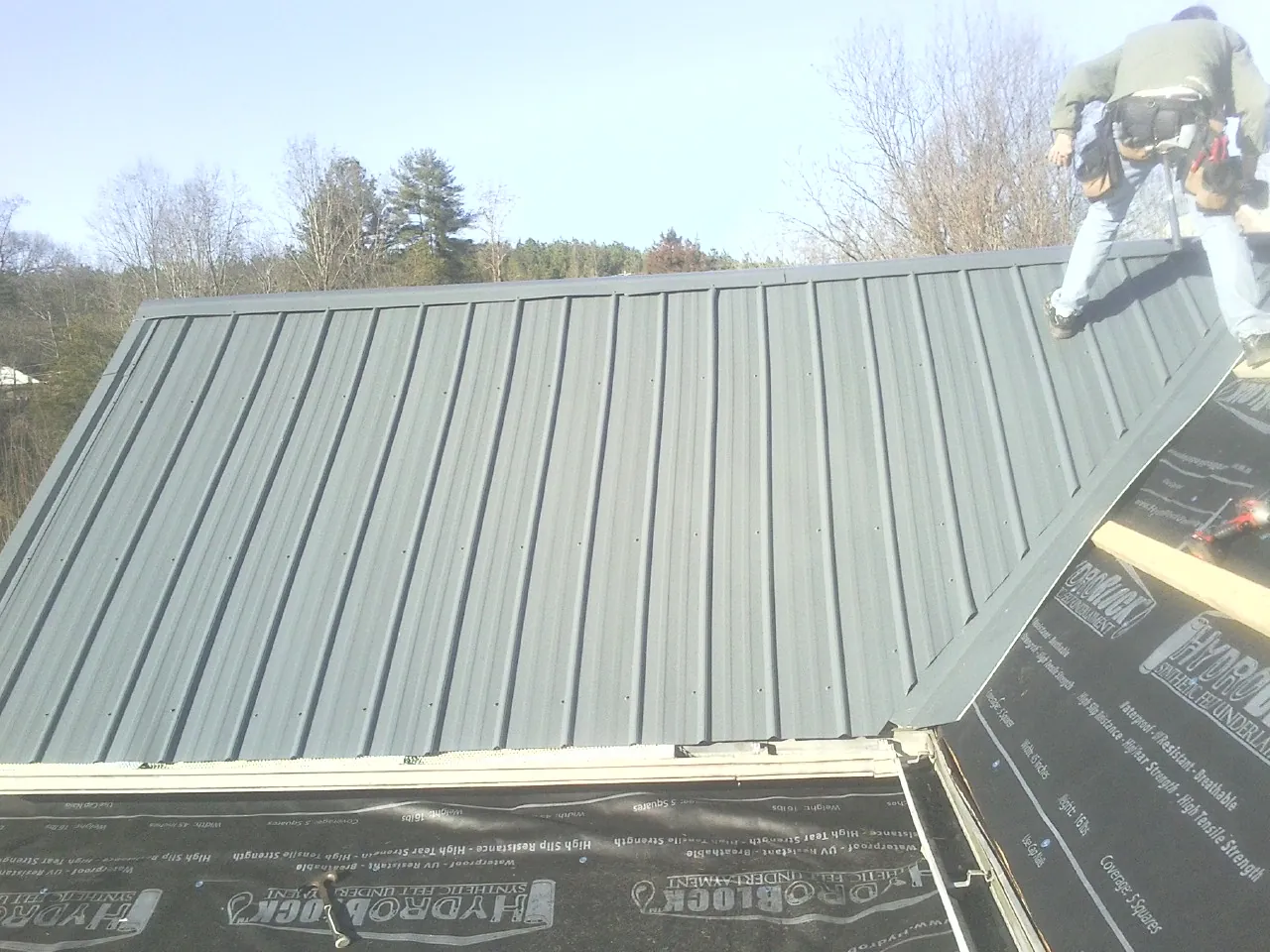 Crew installing dark green standing seam panels over synthetic underlayment in Discovery Bay
