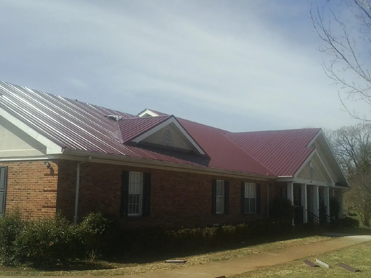Red metal roof with gabled entries on a long brick building, from a Hail Damage Roof Repair job in Discovery Bay