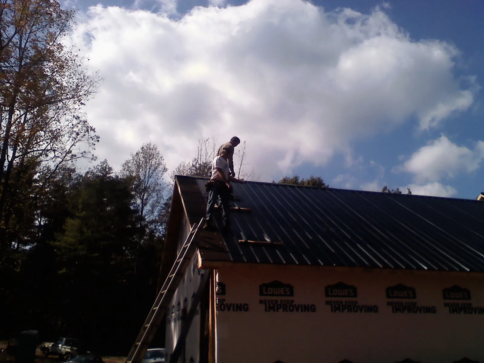 Roofer fastening dark metal panels high against a cloudy sky, from a Roof Inspection job in Discovery Bay