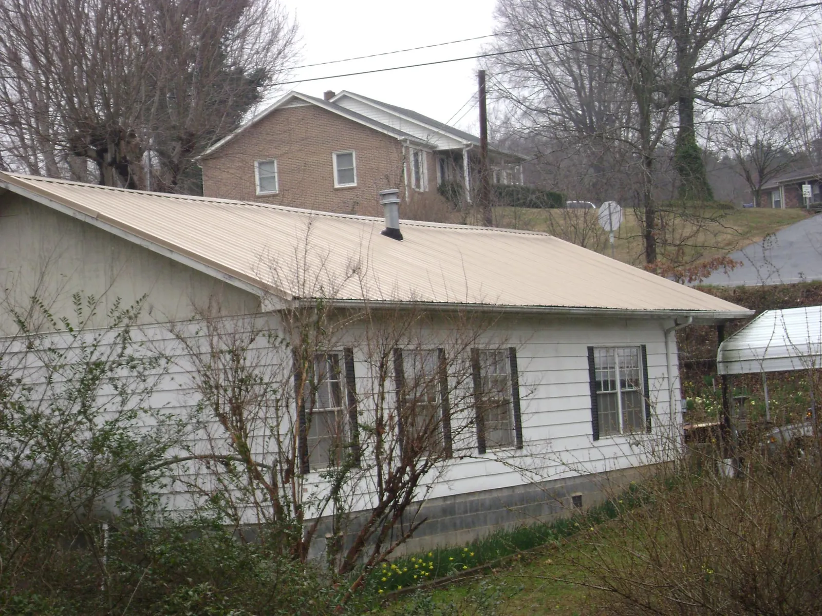 Tan metal roof on a white sided house set into a hillside — Commercial Roofing by Roofing Brothers in Discovery Bay
